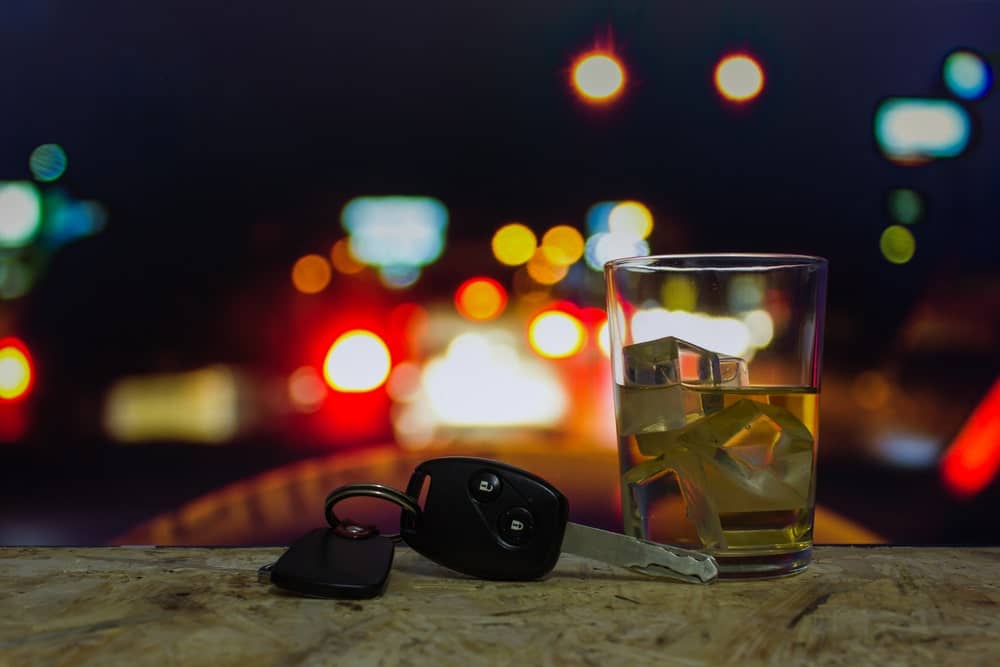 Car Keys And A Glass Of Alcohol On A Curb With Cars In The Foreground